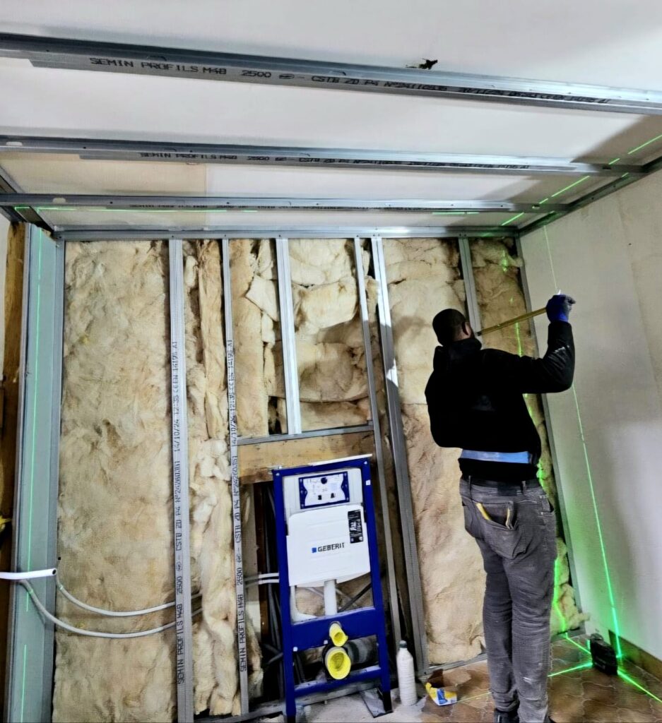 Artisan en train de poser une cloison en plaques de plâtre avec isolation intérieure